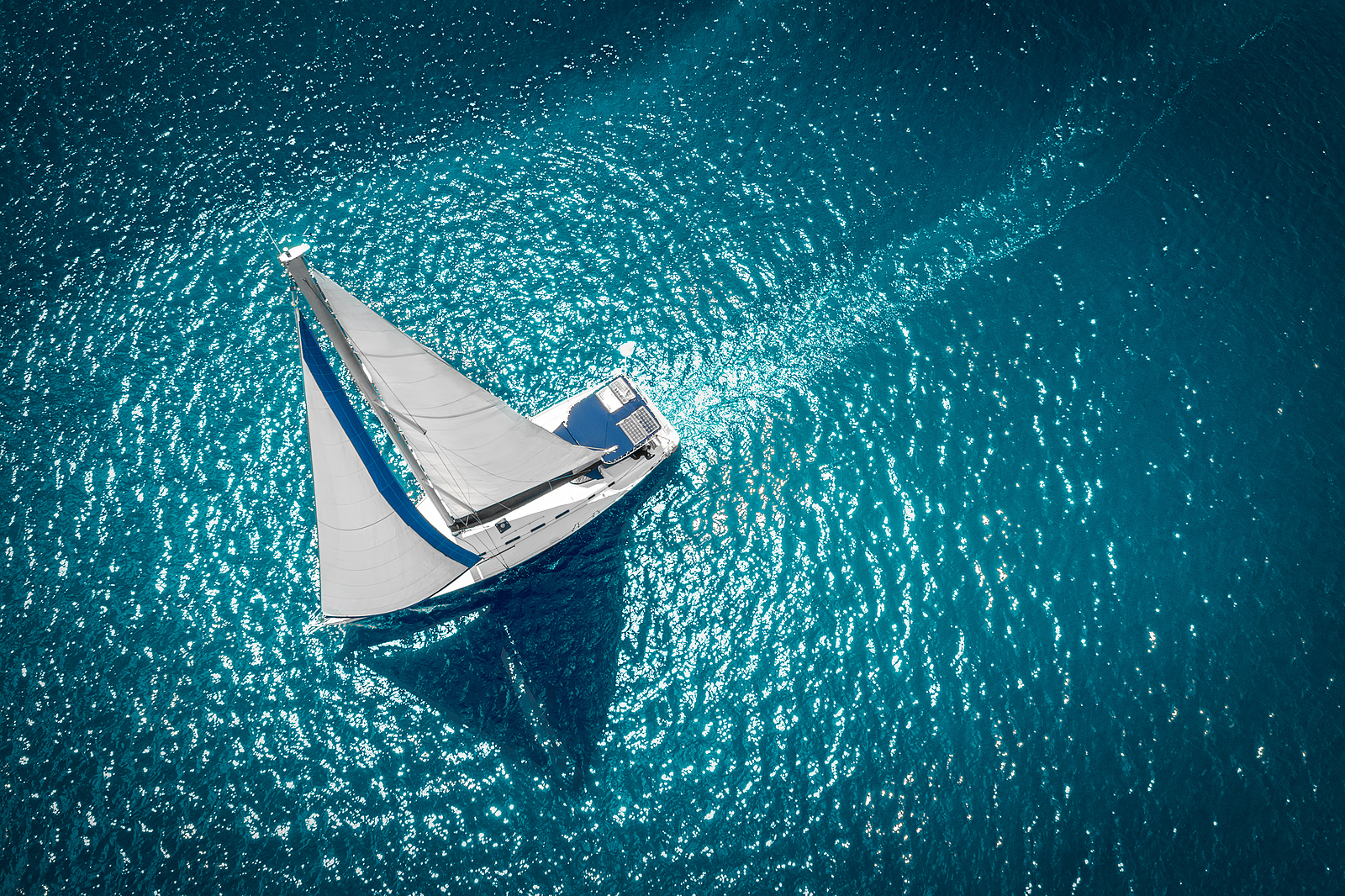 Aerial view of sailboat with white sails on blue waters in windy condition. 
